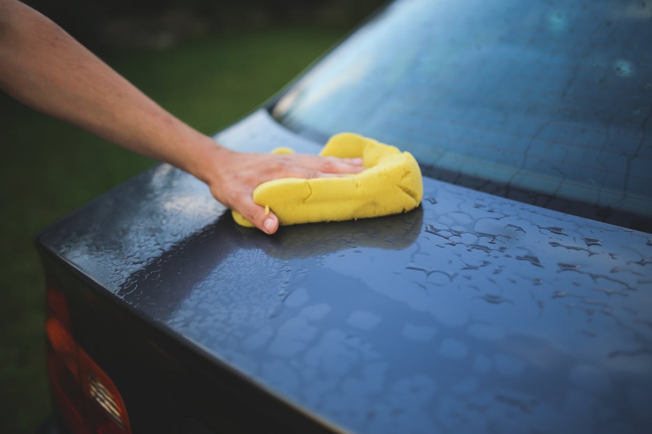 Hand cleaning car with a yellow sponge, showcasing car detailing and washing process.